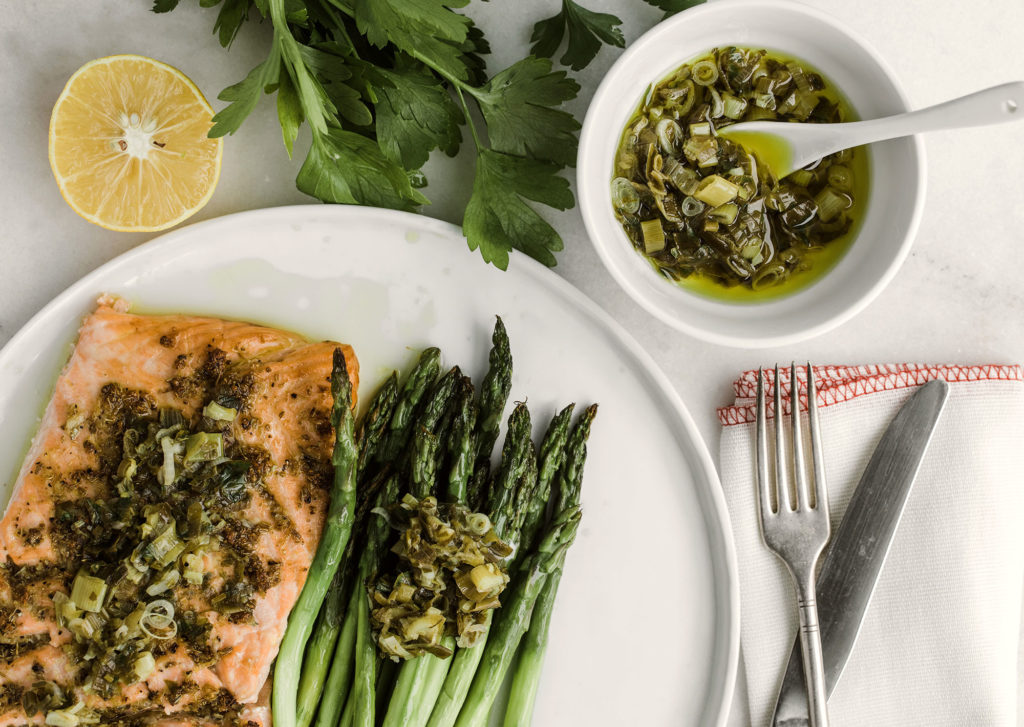 Salmon and asparagus on a plate with a side of scallion sauce